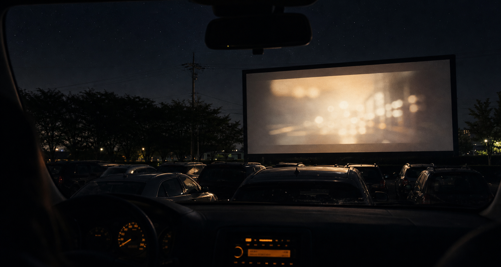 Drive-in cinema view from inside car watching movie on large outdoor screen at night